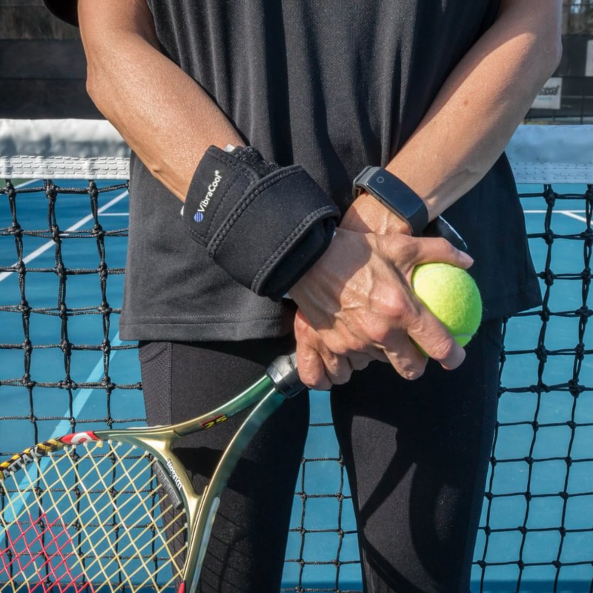 A close-up of a person on a tennis court wearing the VibraCool Easyfit on one wrist and holding a tennis racket and tennis ball. The brace has a white logo that reads 'TENSER'.