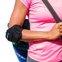 A close-up of a person wearing a VibraCool Easyfit for elbow support brace on their right arm, paired with a pink athletic shirt and a blue bag.